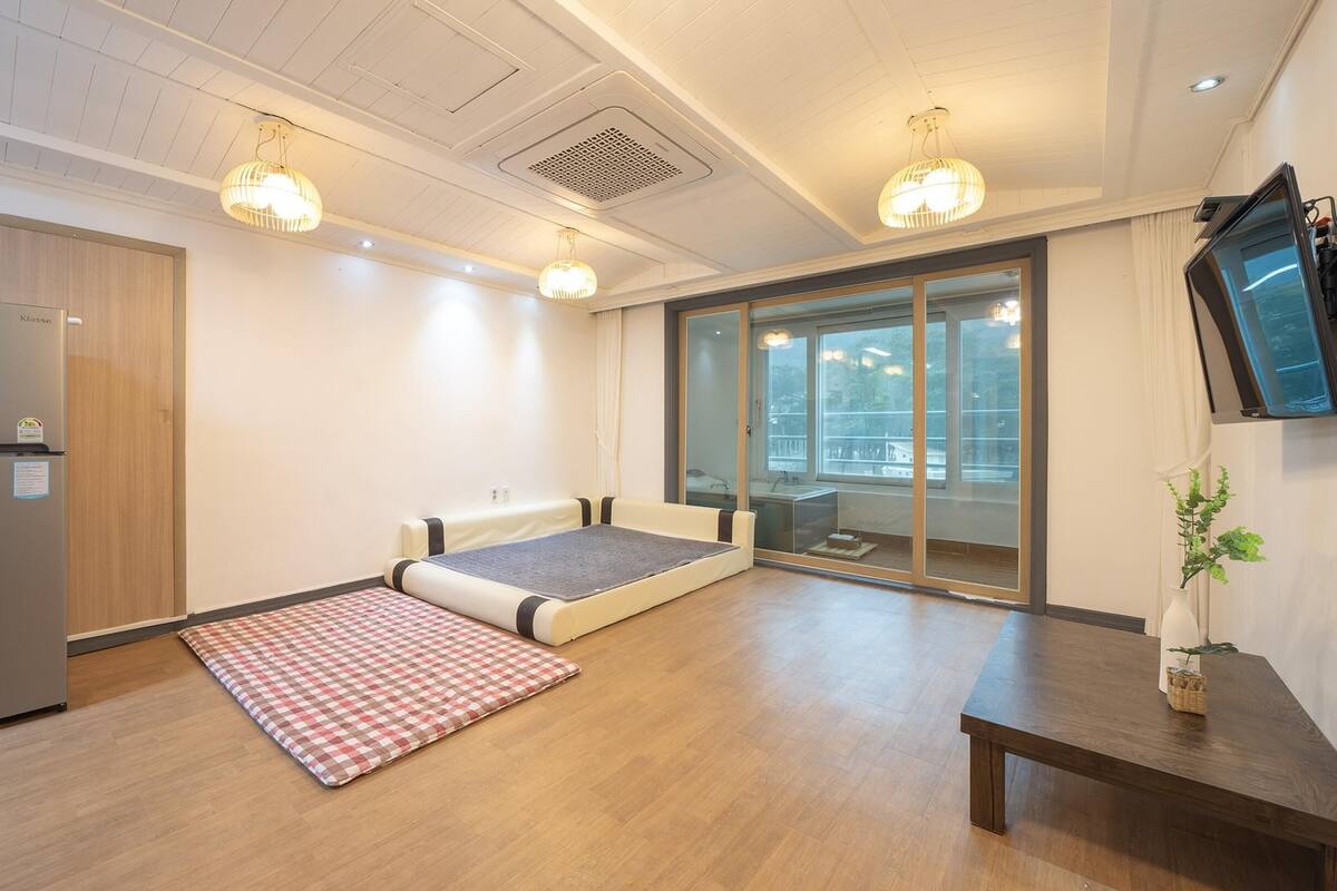 Een compacte kamer met kitchenette, een uitslaapkussen, een klein tafeltje en een groot raam met uitzicht.