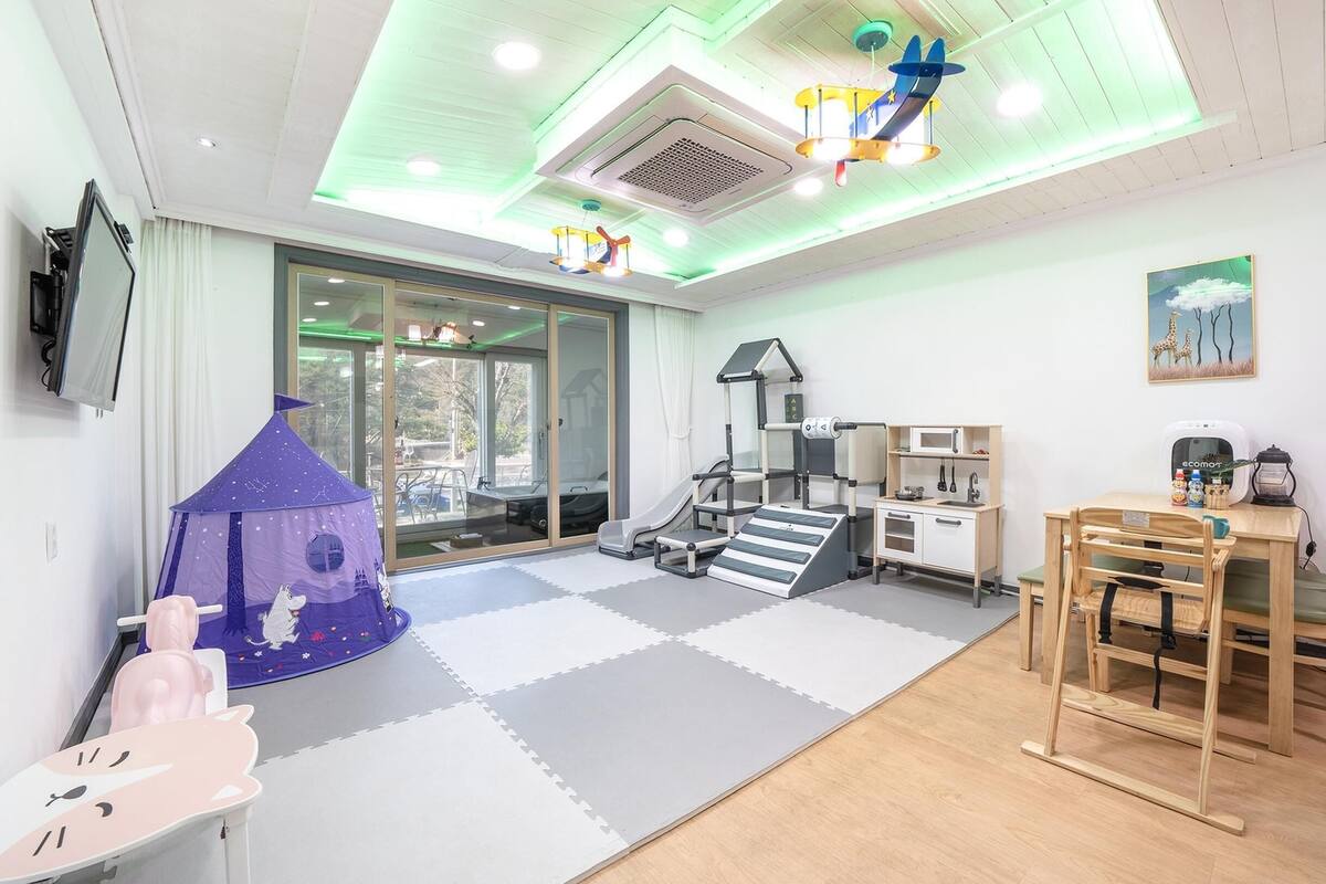 Een kamer met een speelruimte, een bureau met een computer en een eettafel met stoelen.