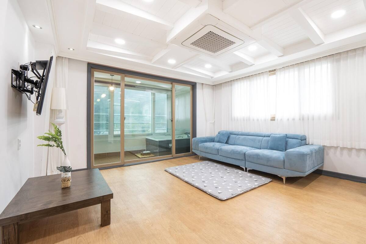 Een moderne woonkamer met een blauwe bank, een houten salontafel en een glazen deur naar een balkon.