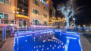 Un hotel con piscina, mobiliario exterior e iluminación con luces colgantes.