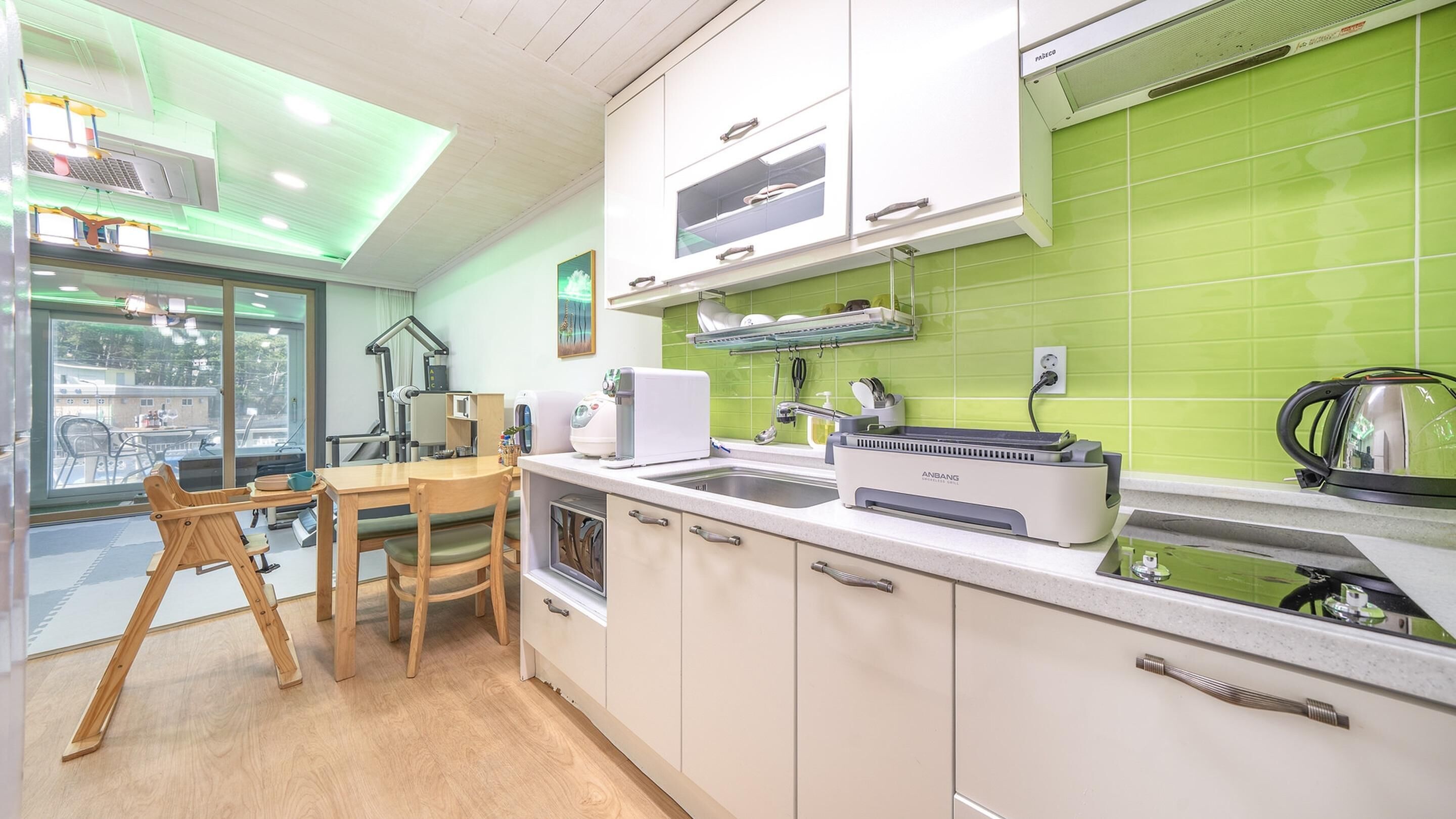 A modern kitchen with white cabinets, a green backsplash, and a dining area with wooden furniture.