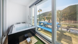 Ein modernes Badezimmer mit einer gläsernen Duschkabine, einer Badewanne und Blick auf einen Außenbereich mit Picknicktisch und Regenbogen-Dekoration.