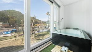 Ein Balkon mit einem gläsernen Whirlpool, Sitzgelegenheiten im Freien und Blick auf einen Swimmingpool und Hügel.