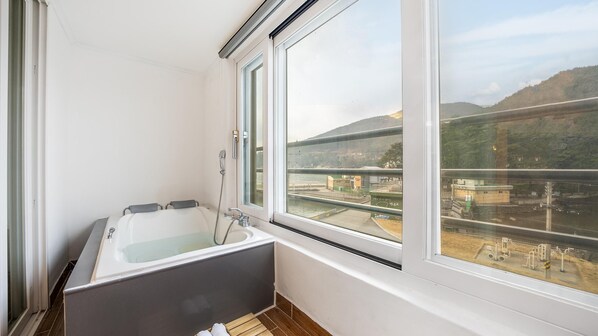 Un baño pequeño con bañera, ventana y vistas a un puente y colinas.