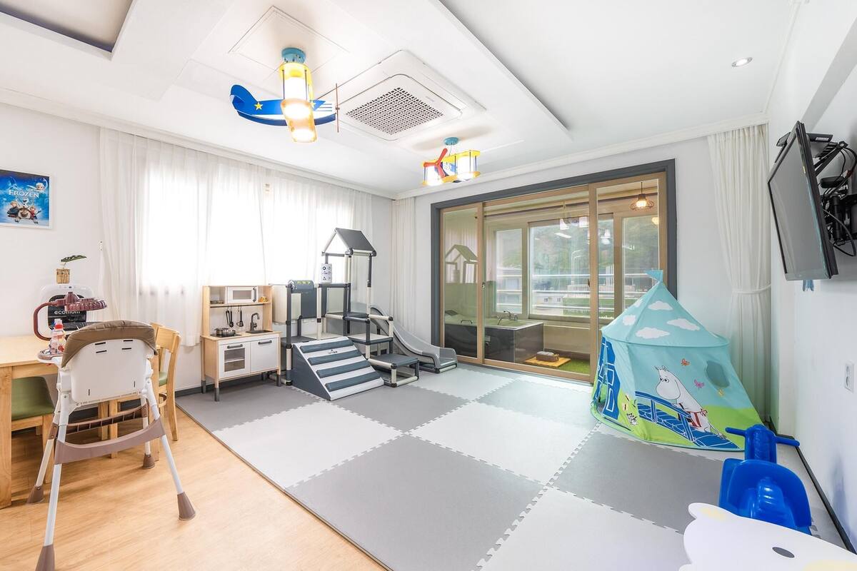 Een kindvriendelijke kamer met een speelruimte, een keuken en een schuifdeur naar een balkon.