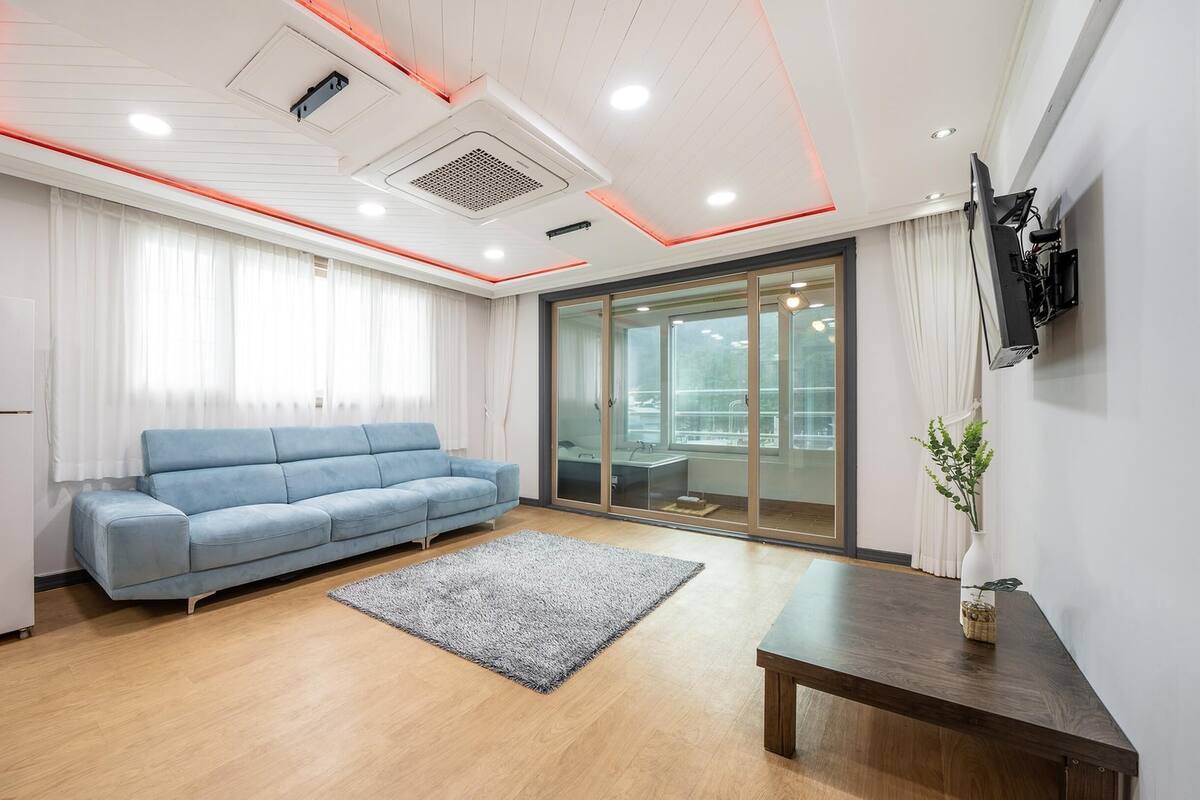 Een moderne kantoorruimte met een blauwe bank, een houten tafel en een glazen deur die leidt naar een balkon.