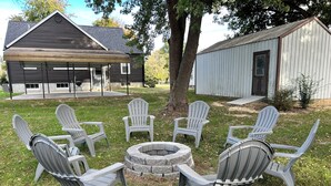 A backyard with Adirondack chairs arranged around a stone fire pit, a wooden deck, and a metal shed. - Charming 3-bedroom house in delightful Advance with AC, WiFi (Advance)