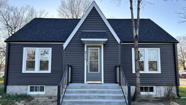 A two-story house with a dark gray exterior, white trim, and a front entrance with a door and steps leading up to it. - Charming 3-bedroom house in delightful Advance with AC, WiFi (Advance)