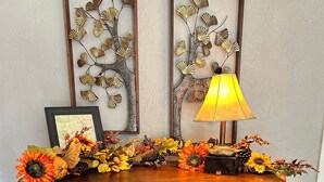 A wooden cabinet with two framed wall decorations, a lamp, and a floral arrangement. - Charming 3-bedroom house in delightful Advance with AC, WiFi (Advance)