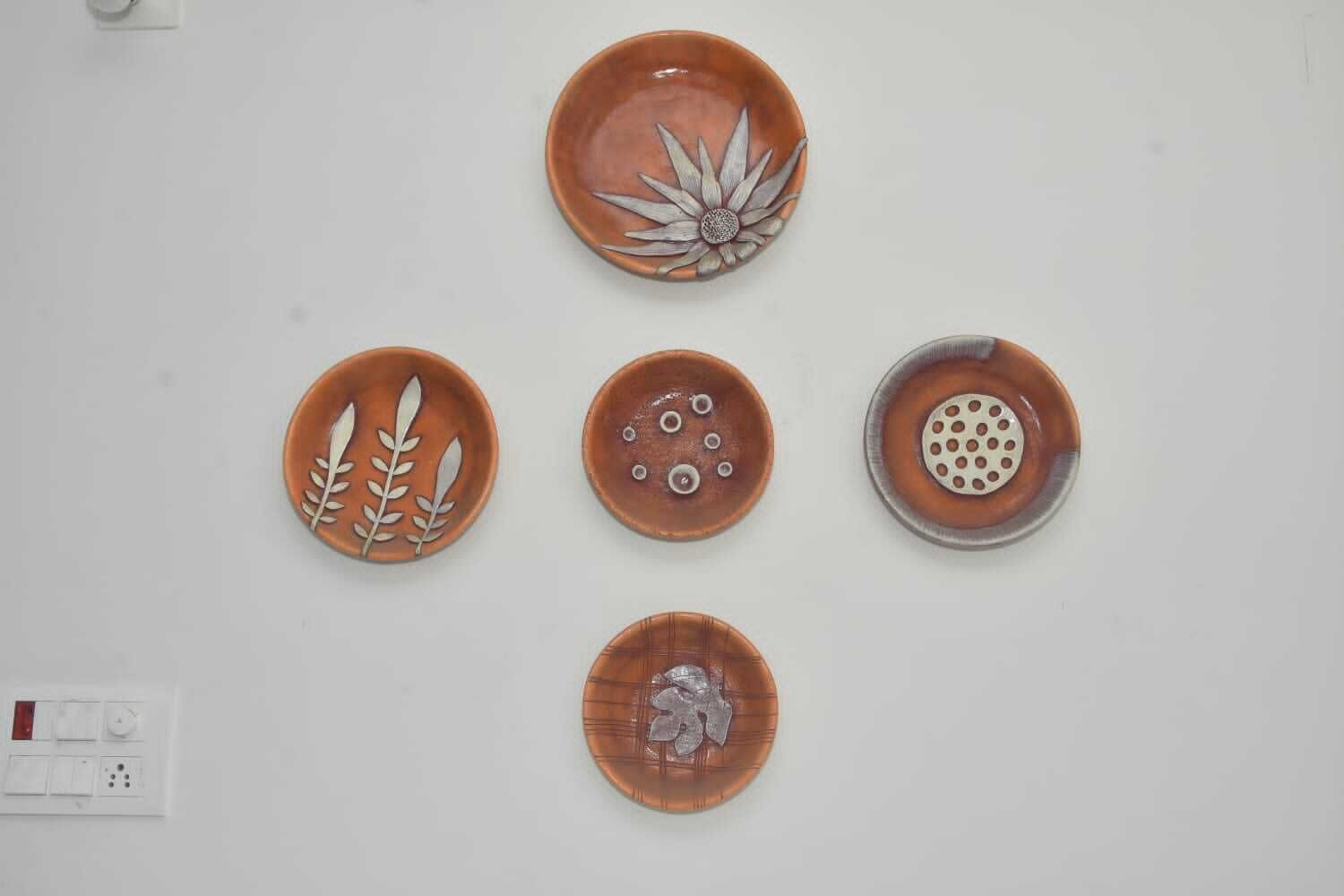 Five ceramic plates with different designs on a white wall.