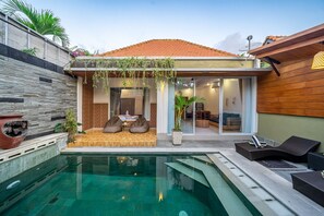 A modern house with a swimming pool, a patio with seating, and a view of the interior. - De Gani Villa (Seminyak)
