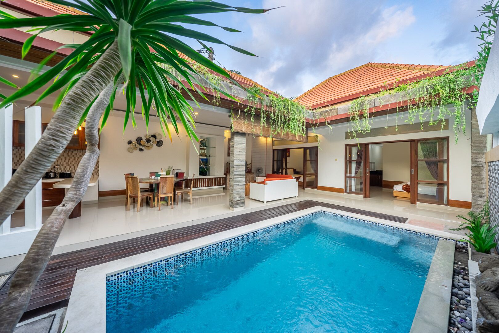 A modern outdoor pool area with a dining setup, a white sofa, and a staircase leading to a covered upper level.