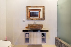 Un baño con lavamanos de piedra, espejo y retrete.