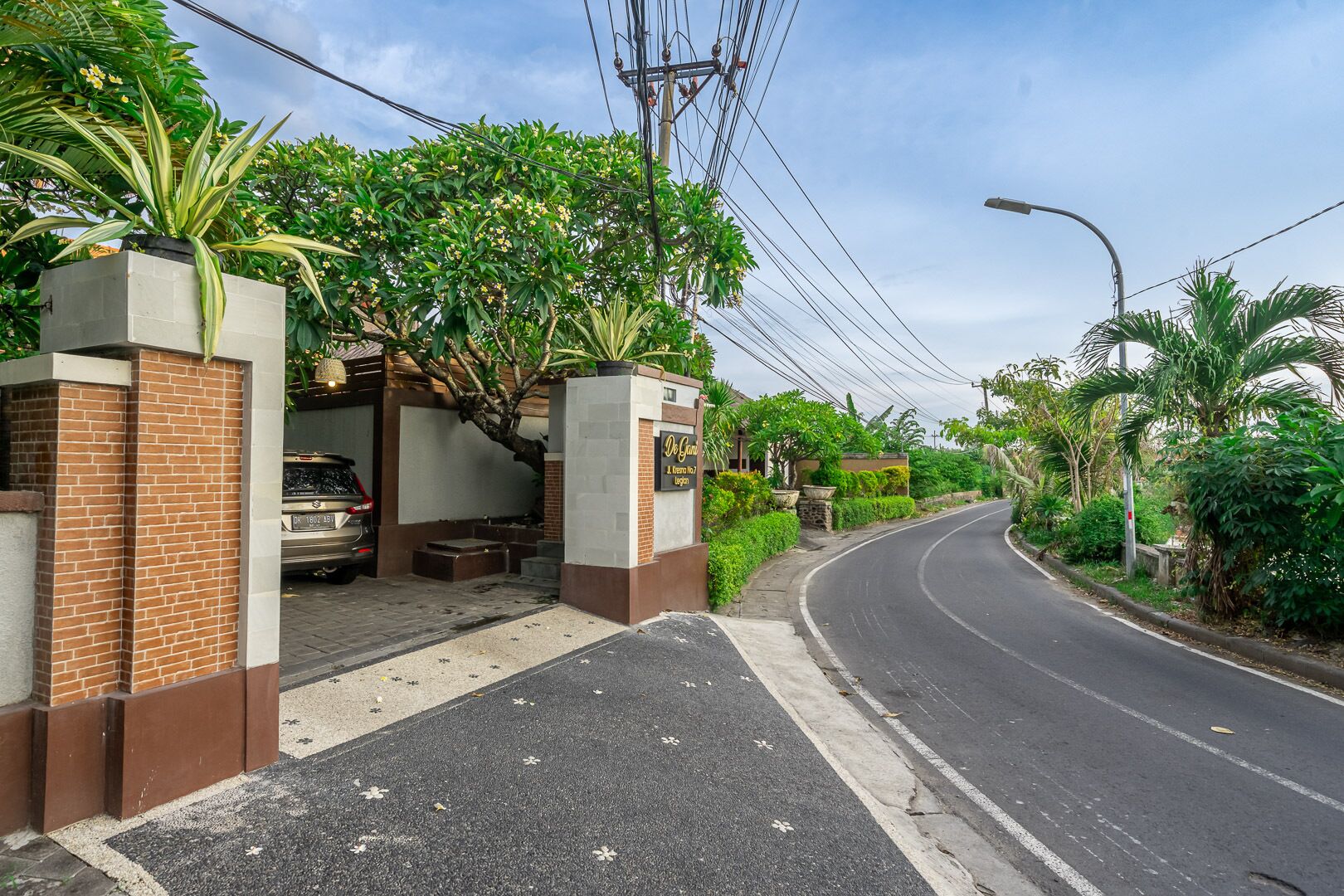 A gated entrance with a car parked inside, surrounded by lush greenery and a curved road.