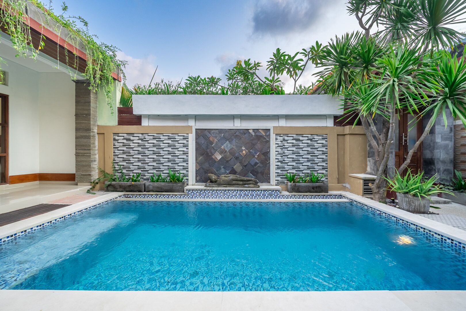 A swimming pool with a tiled edge, surrounded by a stone wall with a patterned design.