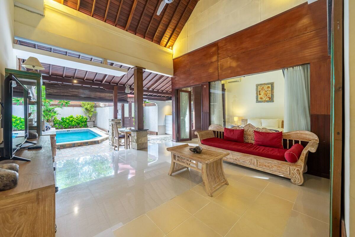 Un amplio salón con piscina, un sofá de madera y una mesa de comedor.