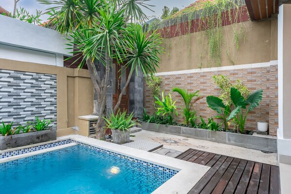 A swimming pool surrounded by plants and a stone wall. - De Gani Villa (Seminyak)