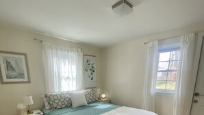 Une chambre à coucher avec un lit, des tables de chevet, une commode, une fenêtre avec des rideaux, une porte et un tapis blanc.