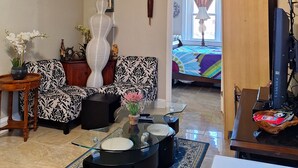 A living room with a sofa, a glass coffee table, a TV, and a ceiling fan.