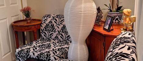 A living room with a large white paper sculpture, a patterned sofa, a small wooden side table, and a vase with flowers.