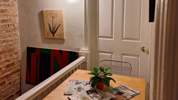 A dining area with a wooden table, chairs, a potted plant, and a wall-mounted light fixture.