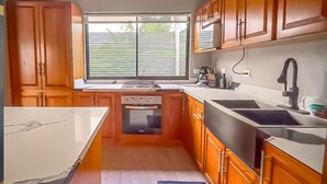 A kitchen with wooden cabinets, a built-in oven, a large window, and a sink. - Modern Uvita Beachhouse by Whale's Tale  (Bahía Ballena)