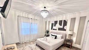 Une chambre à coucher moderne avec un grand lit, un lustre et une vue sur l’extérieur par la fenêtre.