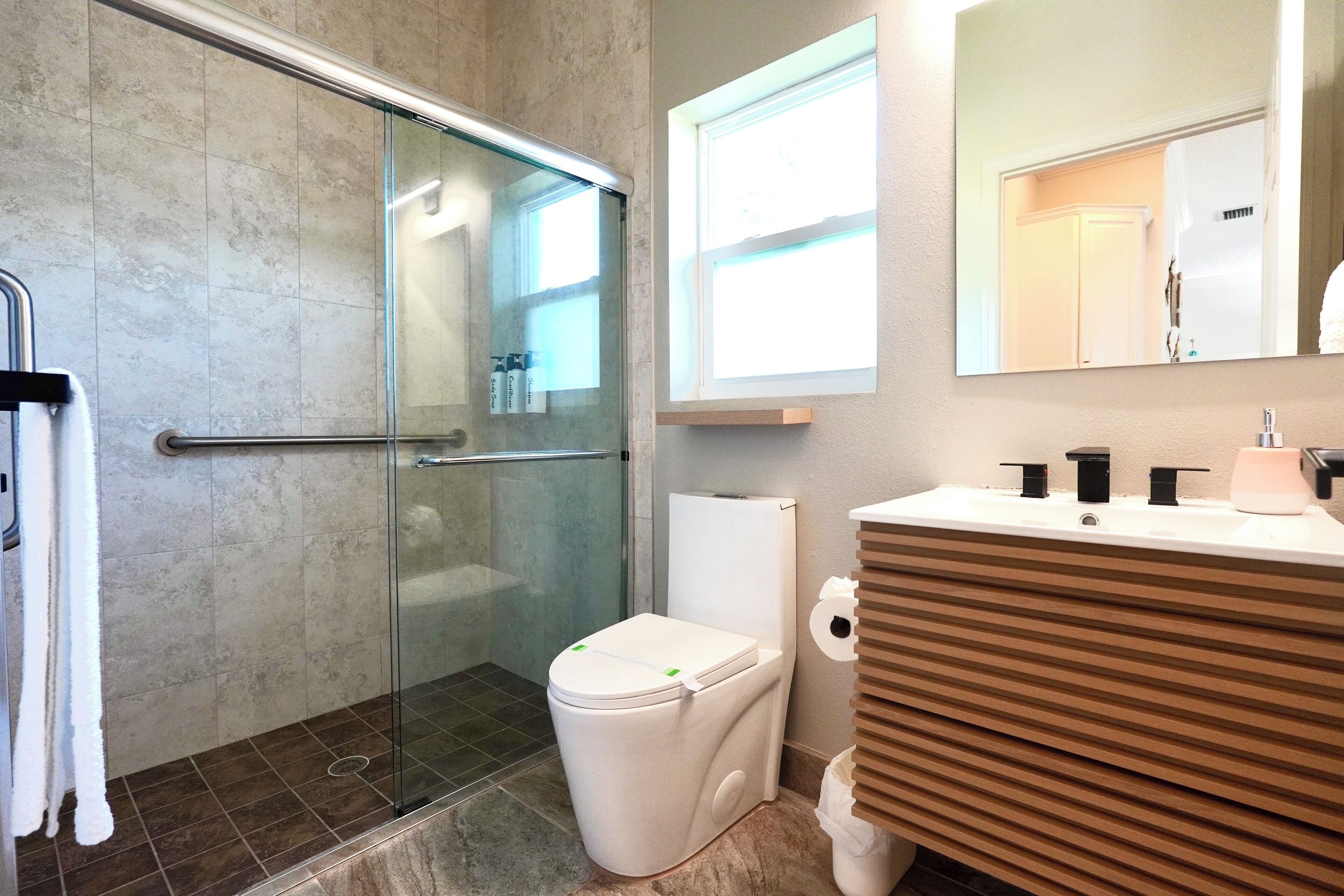 A modern bathroom with a glass shower enclosure, a white toilet, and a vanity with a mirror.