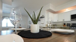 Une cuisine avec des meubles blancs, un îlot central agrémenté d’une plante et deux verres à vin.