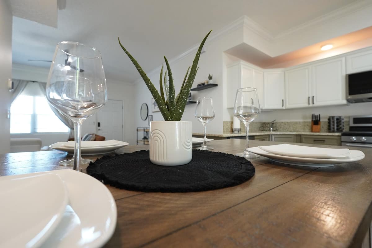 A kitchen with white cabinets, a central island with a plant, and two wine glasses.