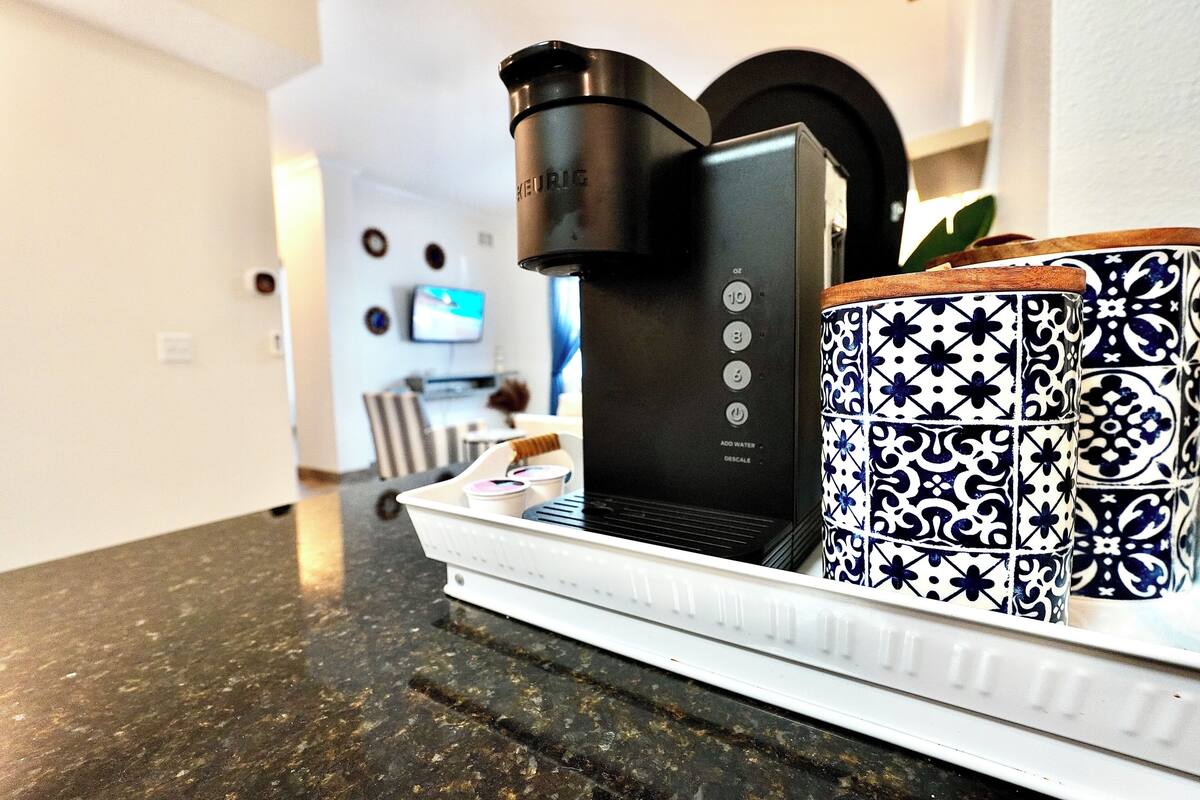 A coffee machine on a tray with a white base, a black coffee pot, and a blue and white patterned mug.