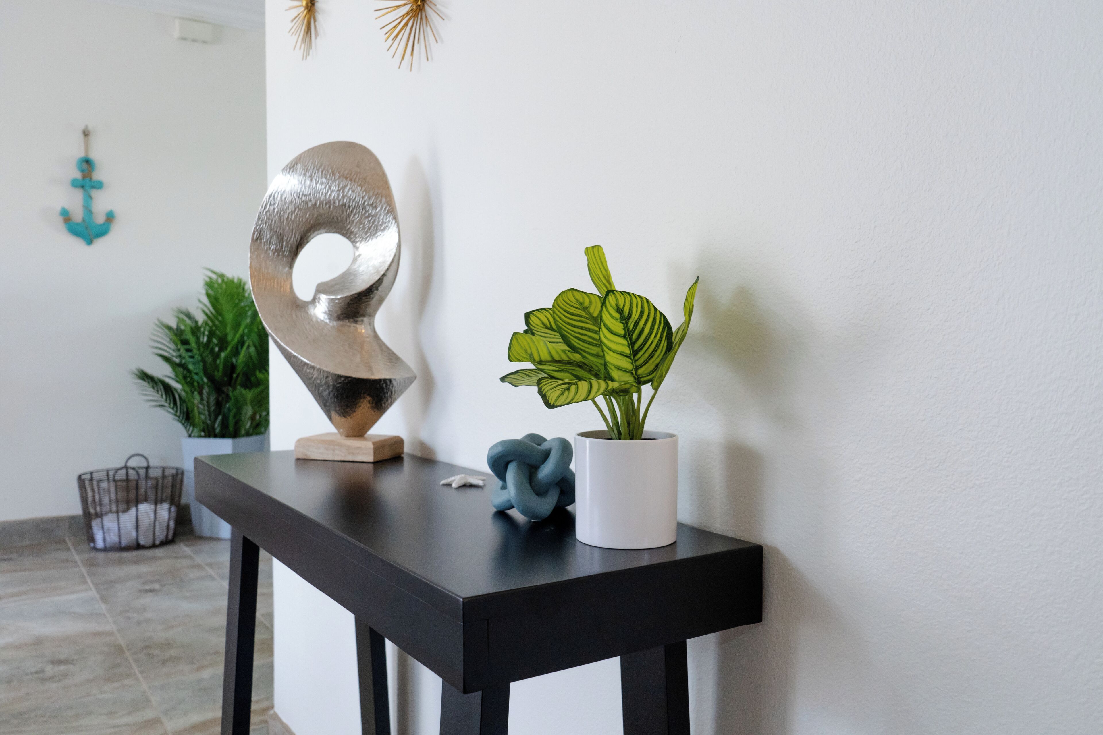 Uma mesa preta com uma escultura de prata, uma planta em vaso e um objeto decorativo azul.