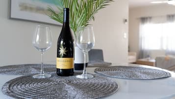 A bottle of Mirassou wine and two glasses on a table with a woven placemat, a potted plant, and a framed picture in a room with a modern design.