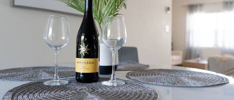 A bottle of Mirassou wine and two glasses on a table with a woven placemat, a potted plant, and a framed picture in a room with a modern design.