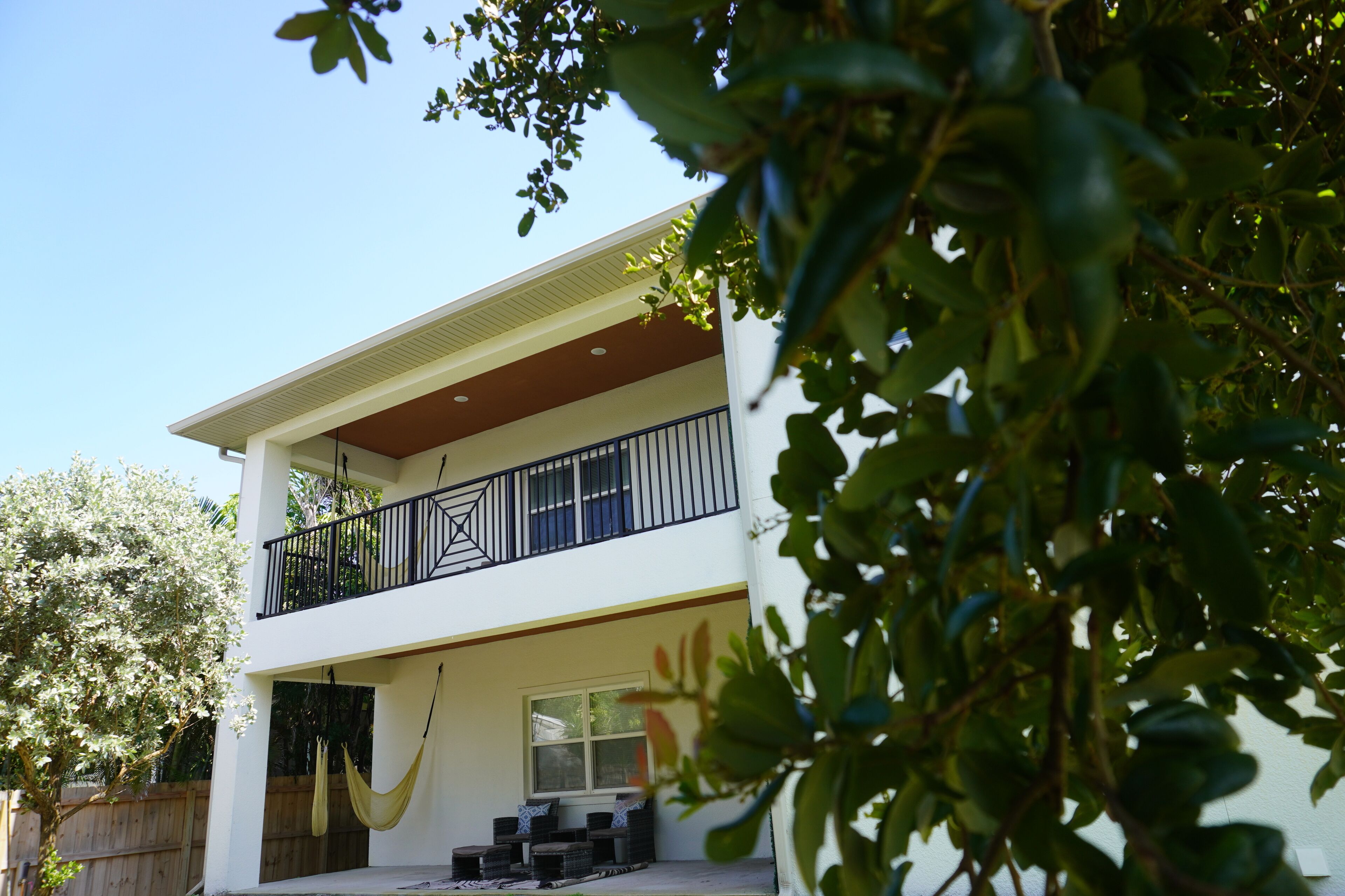 A two-story house with a balcony, a hammock, and a wooden fence.