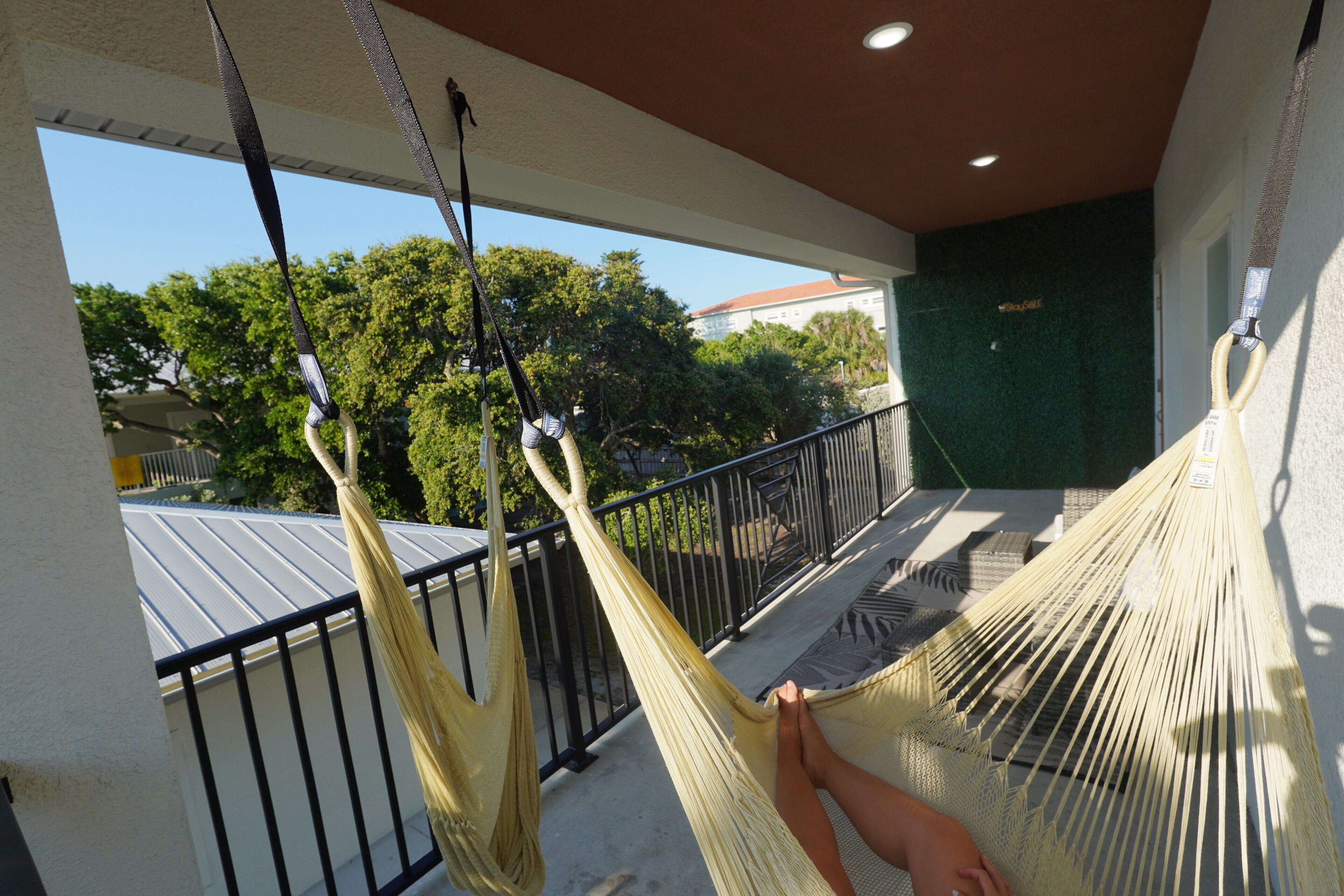 Un hamac sur un balcon, avec vue sur des arbres et un bâtiment en arrière-plan.