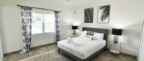 A neatly arranged bedroom with a bed, two bedside lamps, a ceiling fan, and a window with curtains.