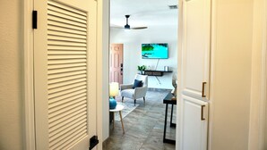 Un couloir avec un ventilateur de plafond, un téléviseur fixé au mur, une chaise, une table et une porte.