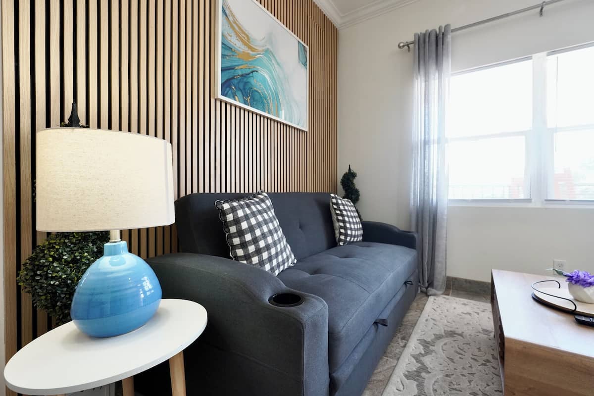 A modern living room with a grey sofa, a blue lamp, and a painting on the wall.
