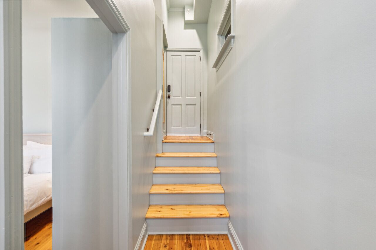 A narrow hallway with a wooden staircase leading to a white door.