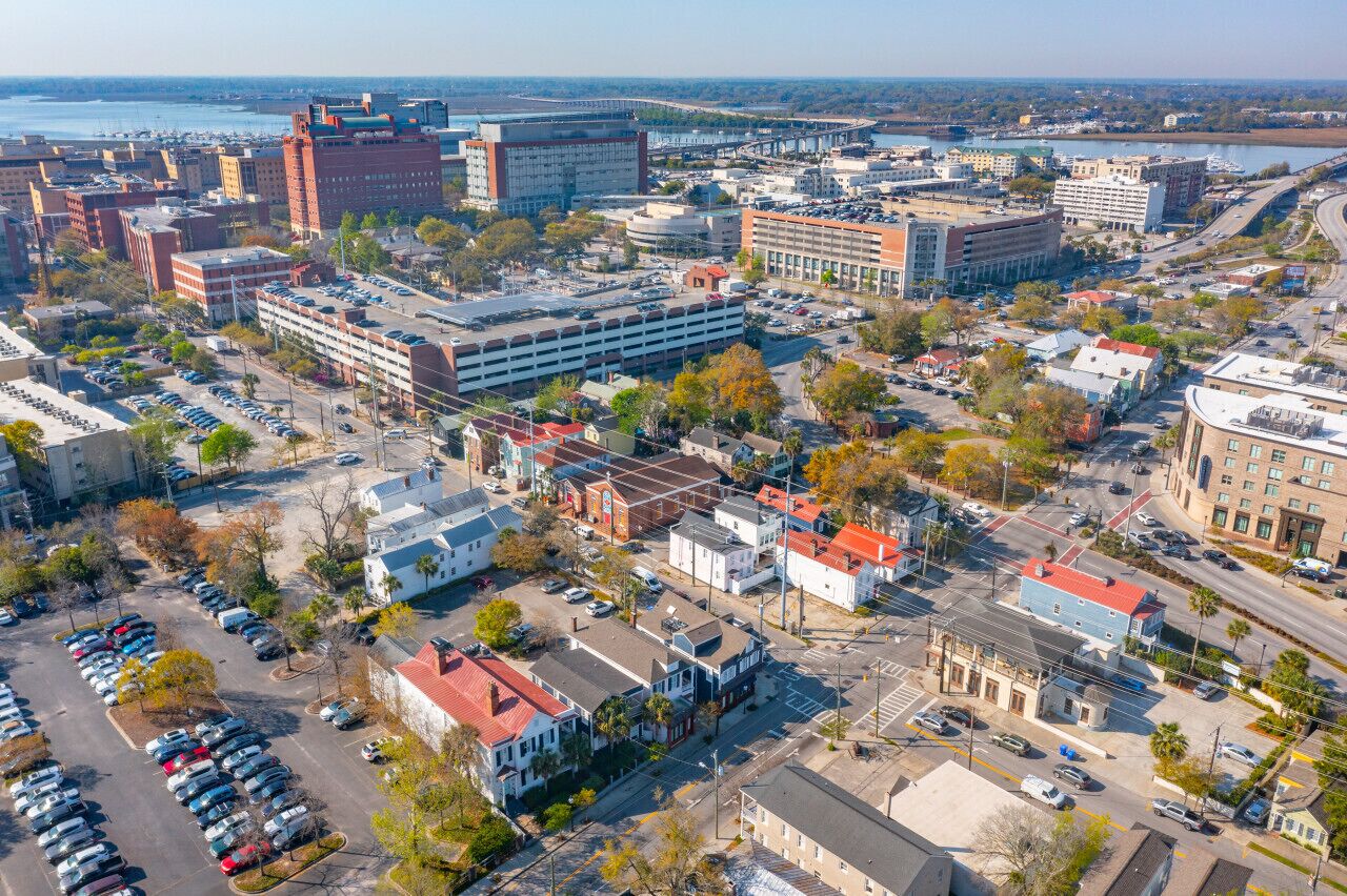 An aerial view of a city with a mix of commercial and residential buildings, a parking lot, and a bridge in the background.