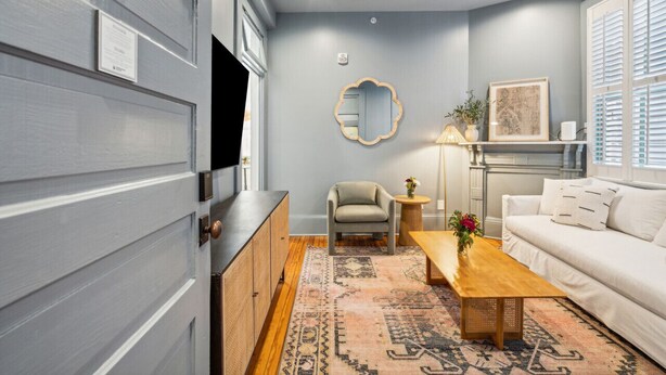 A room with a grey door, a ceiling fan, a sofa, a coffee table, a chair, a mirror, and a patterned rug.