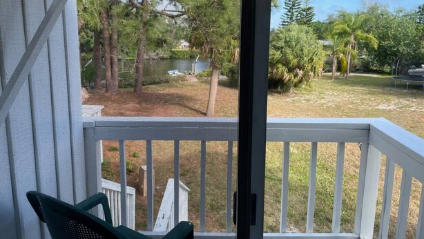 A balcony with a view of a backyard, a white railing, and a green chair.