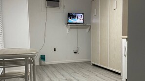 A room with a ceiling fan, a TV mounted on a wall, a small shelf, and a wooden floor.