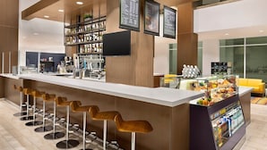 A modern bar area with a long counter, multiple stools, and a display case with food items. - Anaheim | Couples Theme Park Getaway | Pool + Parks (Anaheim)