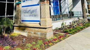 A Wyndham Courtyard Restaurant & Bar with a modern building facade, palm trees, and a clear blue sky. - Anaheim | Couples Theme Park Getaway | Pool + Parks (Anaheim)