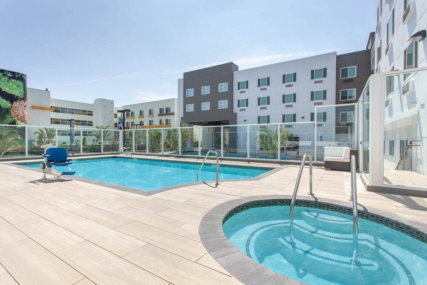 Un espace piscine aménagé sur le toit, comprenant deux piscines, un fauteuil de relaxation bleu et une rambarde en verre.