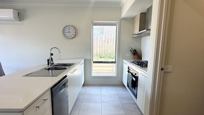 A modern kitchen with a dishwasher, sink, and stove. There is a window with a view of a backyard. - Spacious Coastal Oasis - 10 min to Torquay, 10 min to Geelong ! (Mount Duneed)