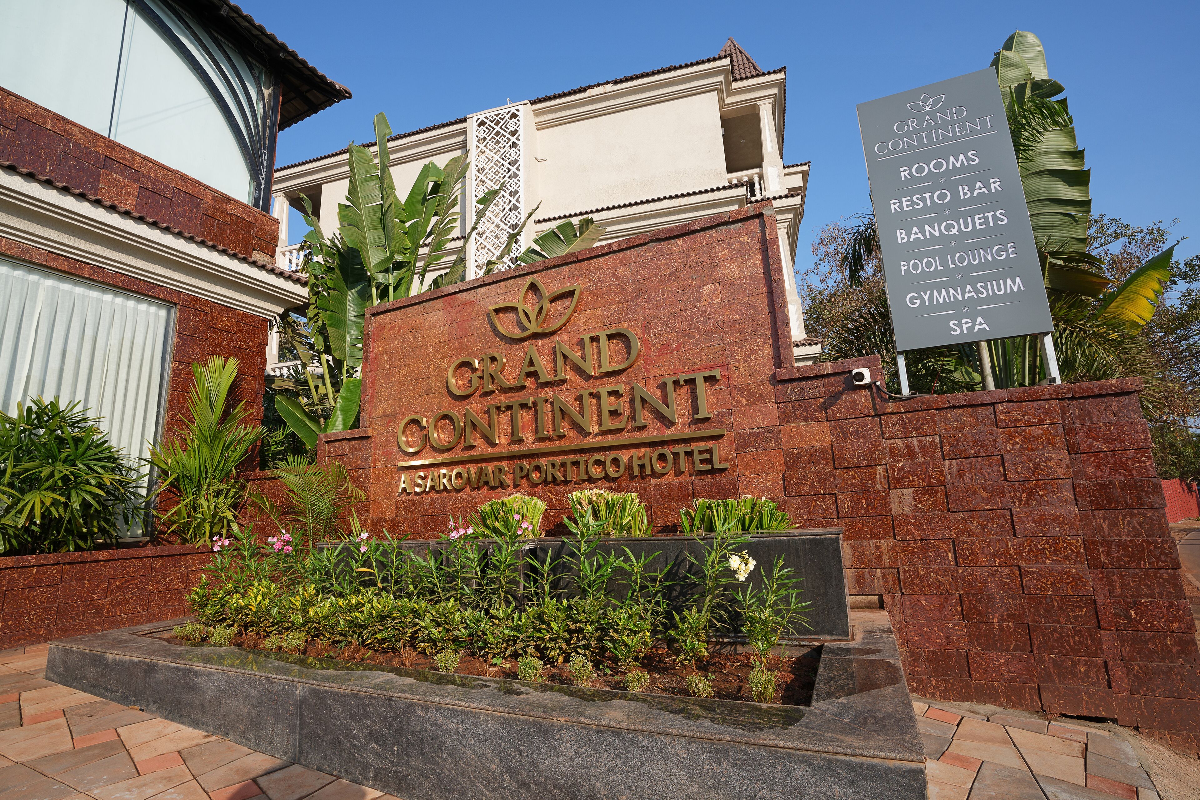A sign for Grand Continent Sarovar Portico Hotel listing amenities like rooms, a restaurant bar, banquets, a pool lounge, a gymnasium, and a spa.