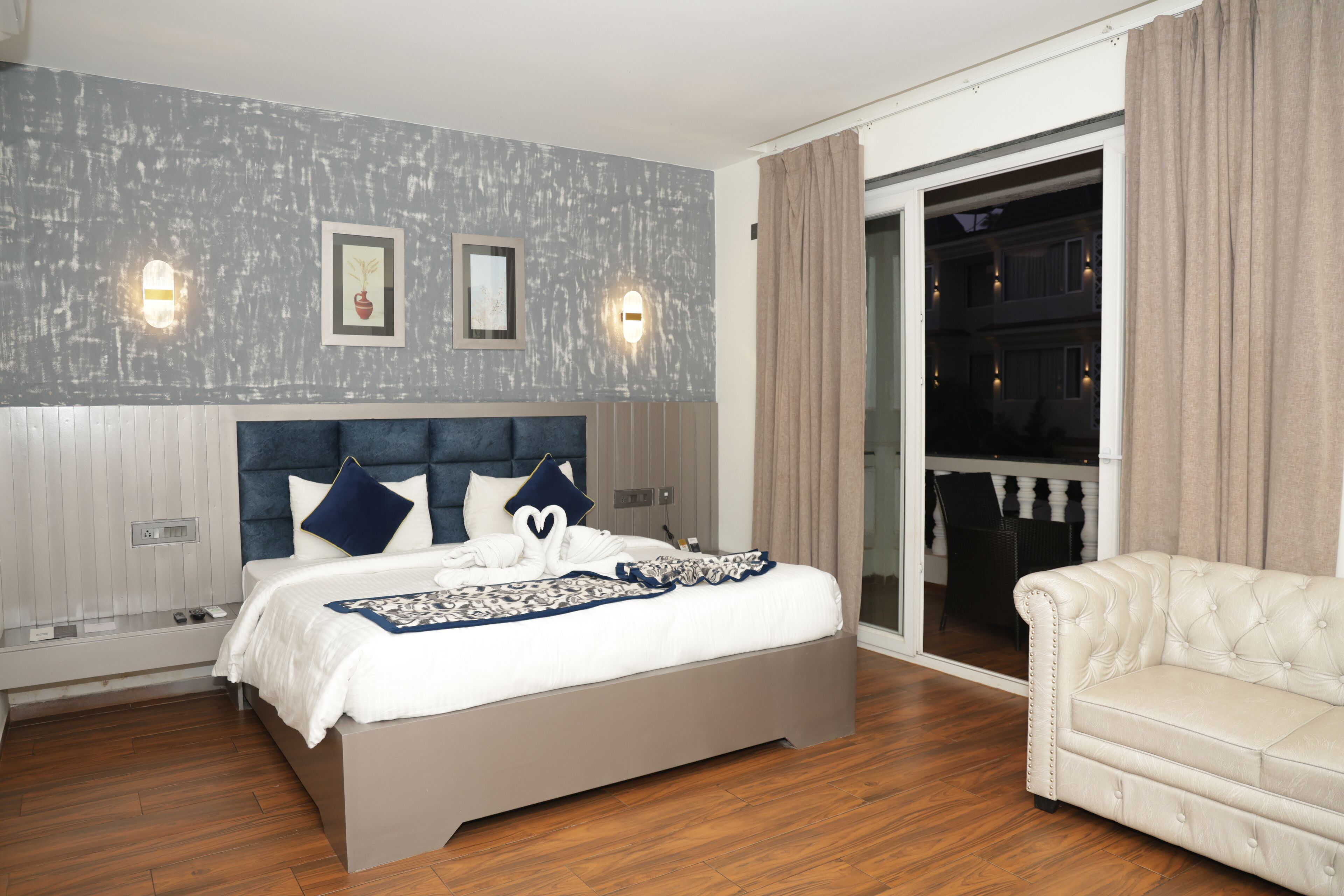 A modern bedroom with a large bed, a sofa, and a balcony with curtains.